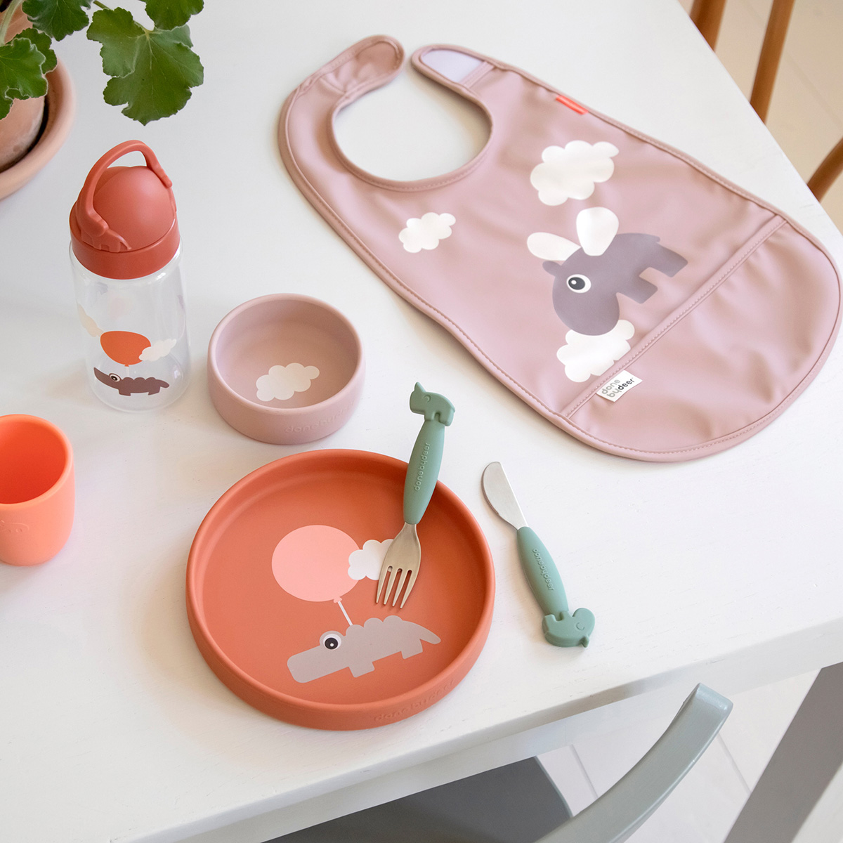 Bavoir Done by Deer rose à côté d’un set repas bébé assorti.