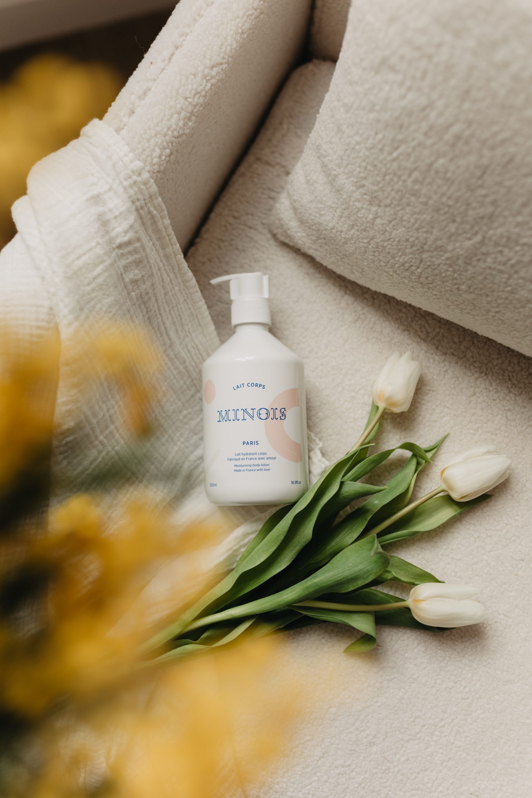 Lait hydratant bébé Minois Paris avec fleurs blanches et tissu beige.