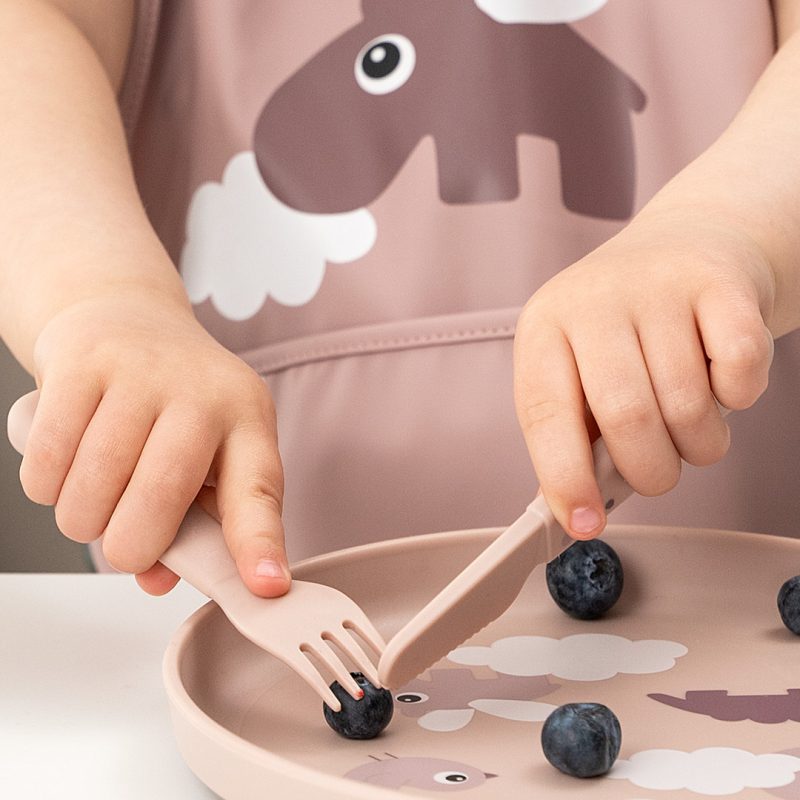 Enfant utilise une assiette rose Done By Deer avec rebords pour manger des myrtilles en autonomie