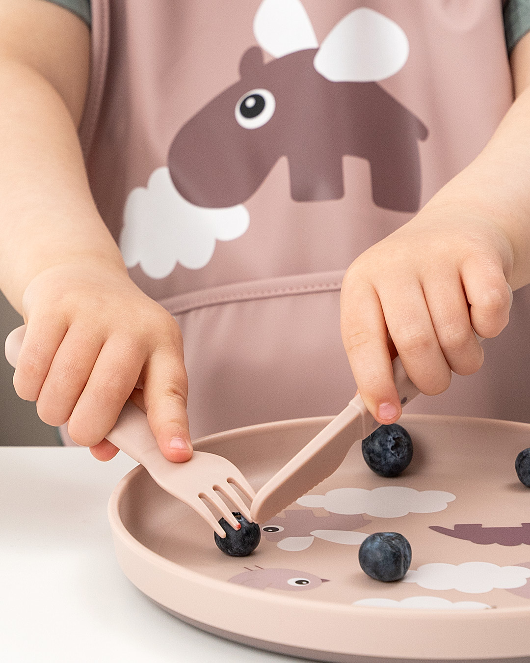 Enfant utilise une assiette rose Done By Deer avec rebords pour manger des myrtilles en autonomie