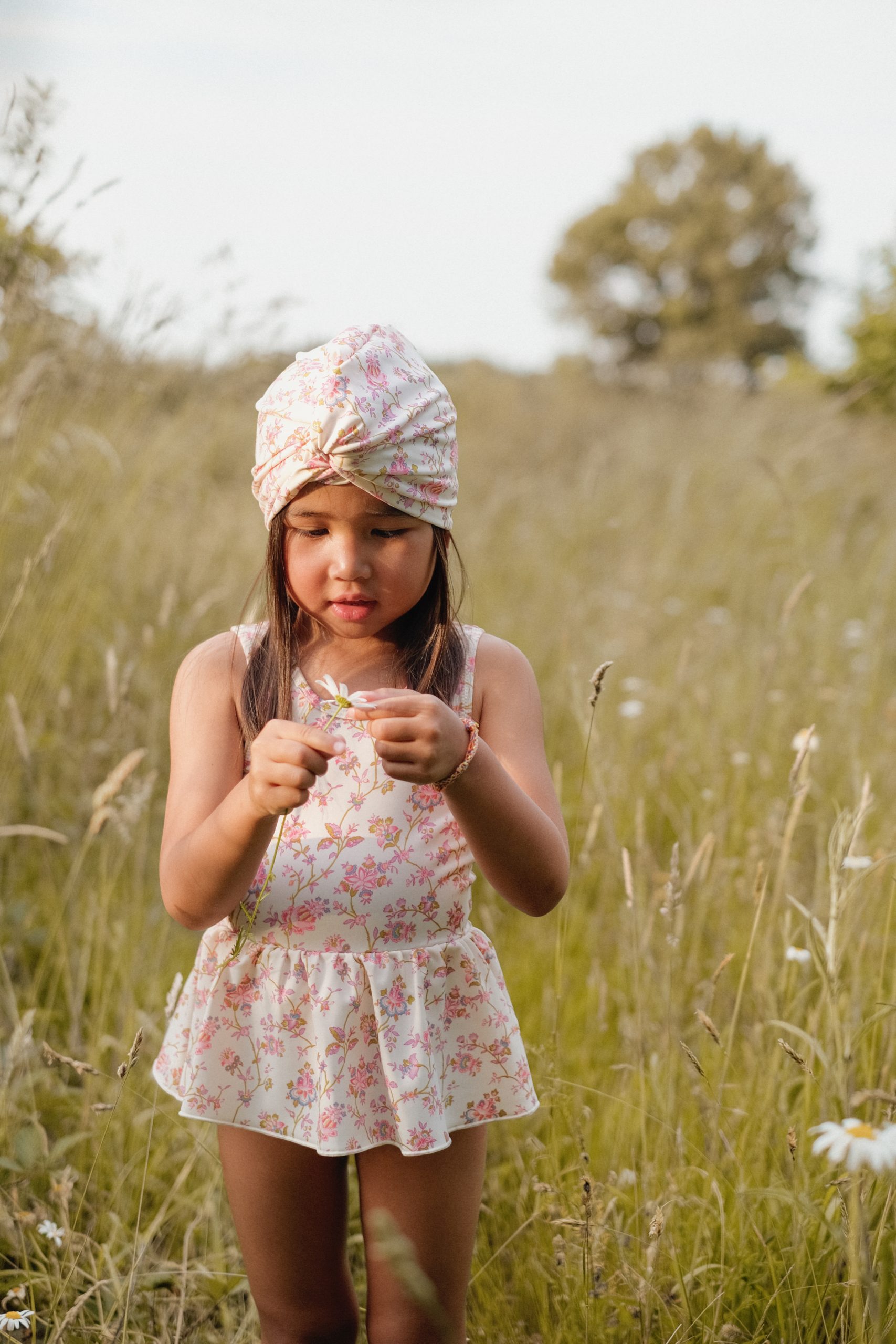 Petite fille dans un champ portant un maillot de bain bébé fille rose une pièce Kalinda avec jupette