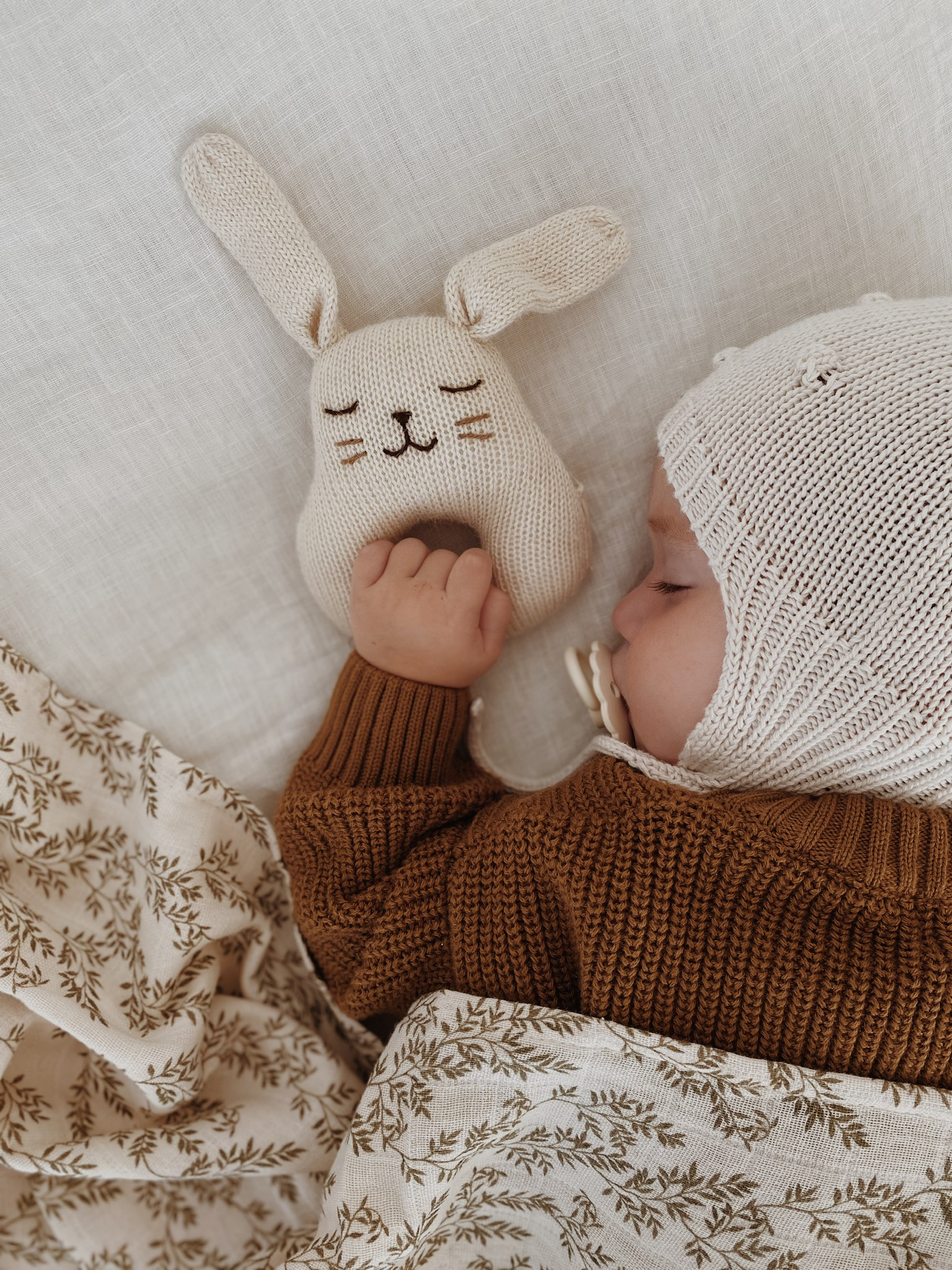 Bébé dormant avec un hochet lapin écru en laine tricotée Main Sauvage dans la main
