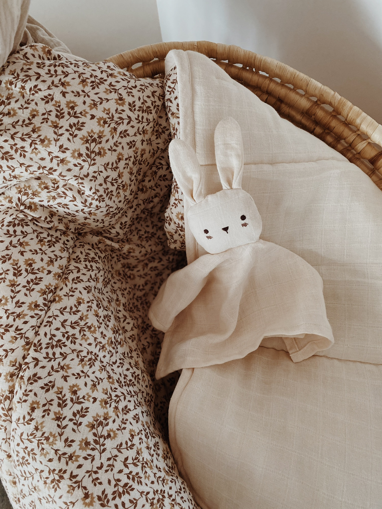 Doudou lange Lapin écru Main Sauvage dans un couffin sur draps fleuris – lumière naturelle