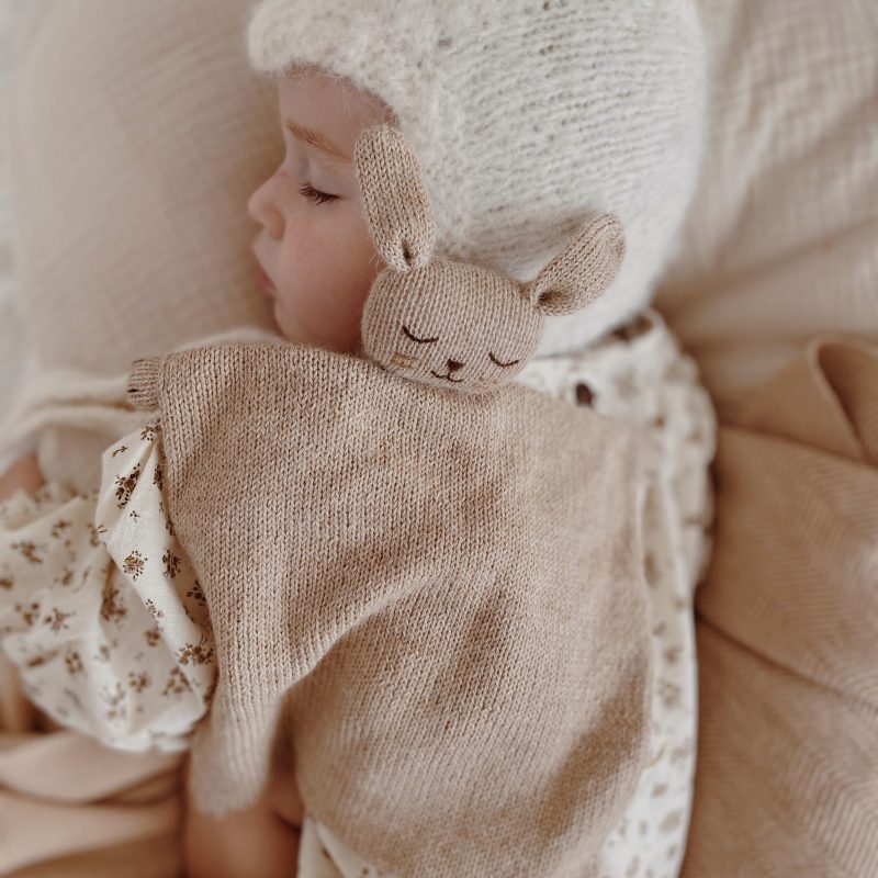 Bébé endormi de profil avec le doudou plat Lapin sable Main Sauvage posé sur lui – scène paisible