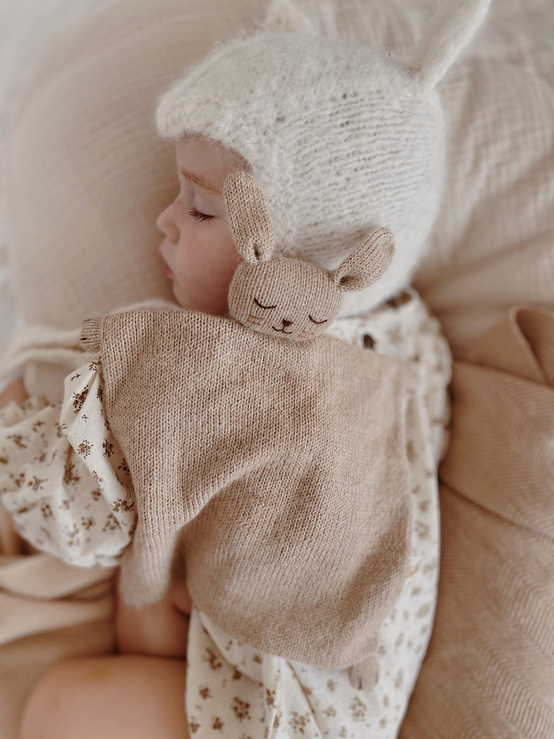 Bébé endormi de profil avec le doudou plat Lapin sable Main Sauvage posé sur lui – scène paisible