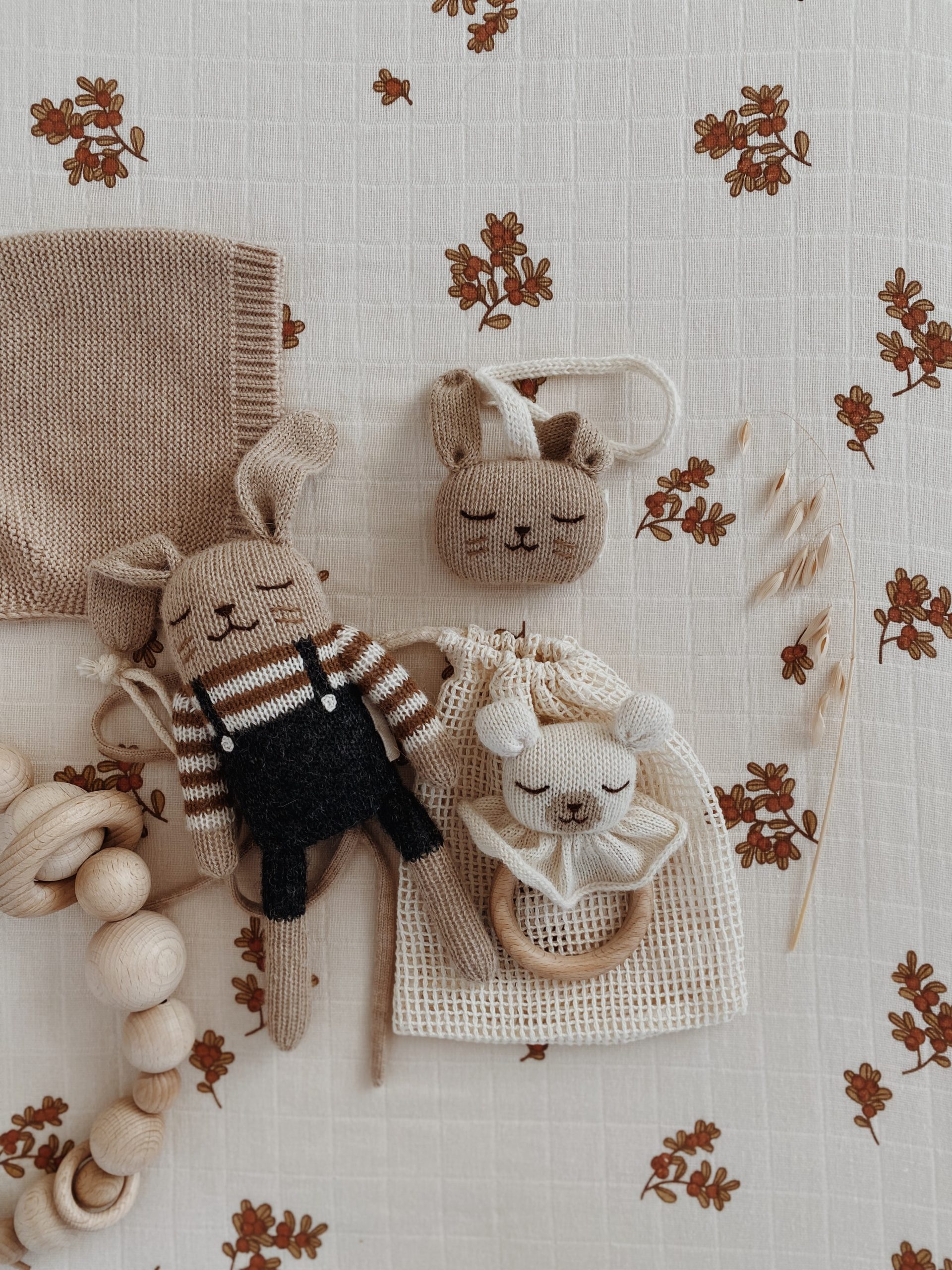 Doudou Lapin salopette noire Main Sauvage posé sur un matelas avec un anneau de dentition, un jouet en bois et un lange – tons naturels assortis