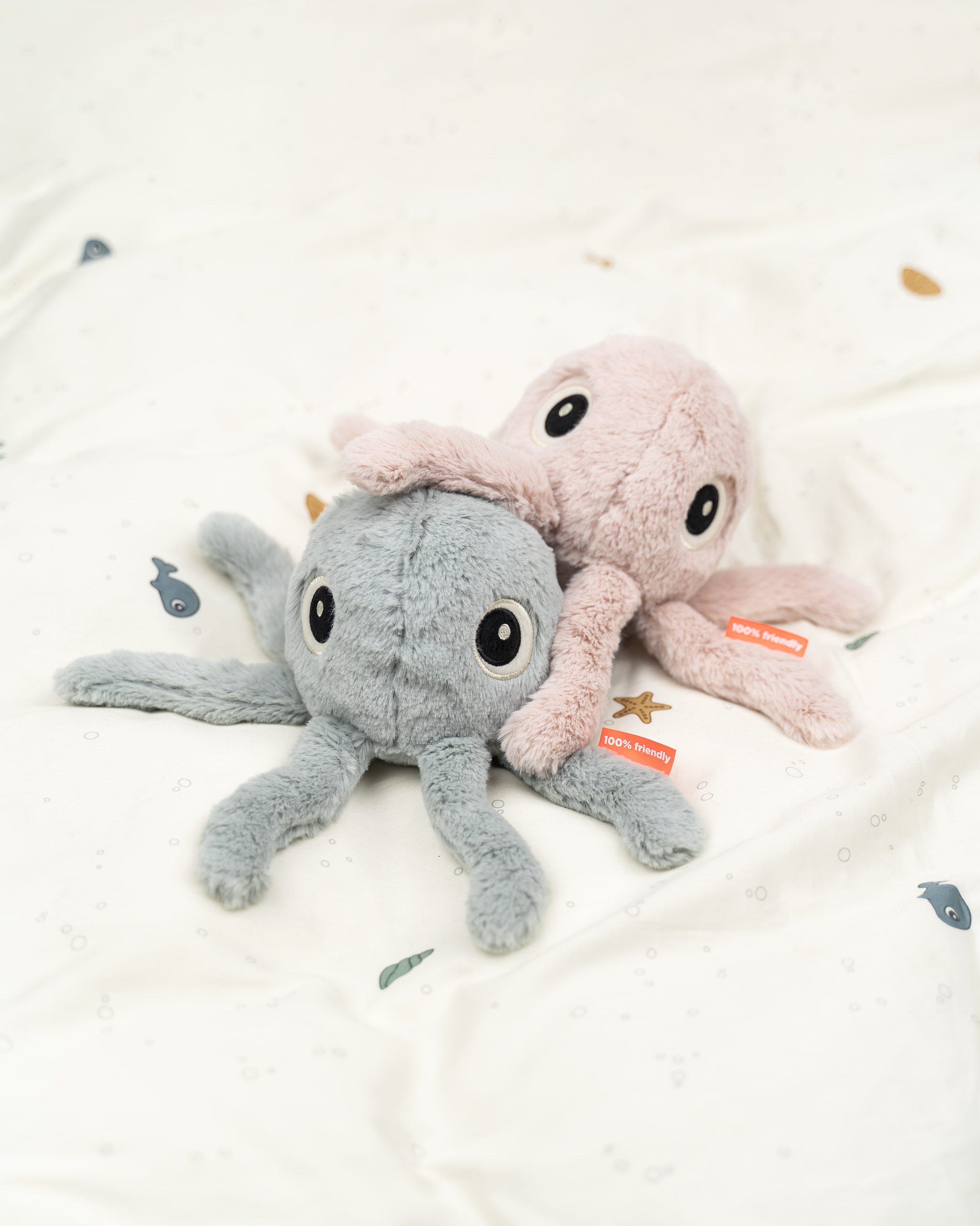 Peluche Jelly la méduse rose poudré posée sur un lit, au-dessus d’une autre peluche Jelly grise – Done by Deer – ambiance douce