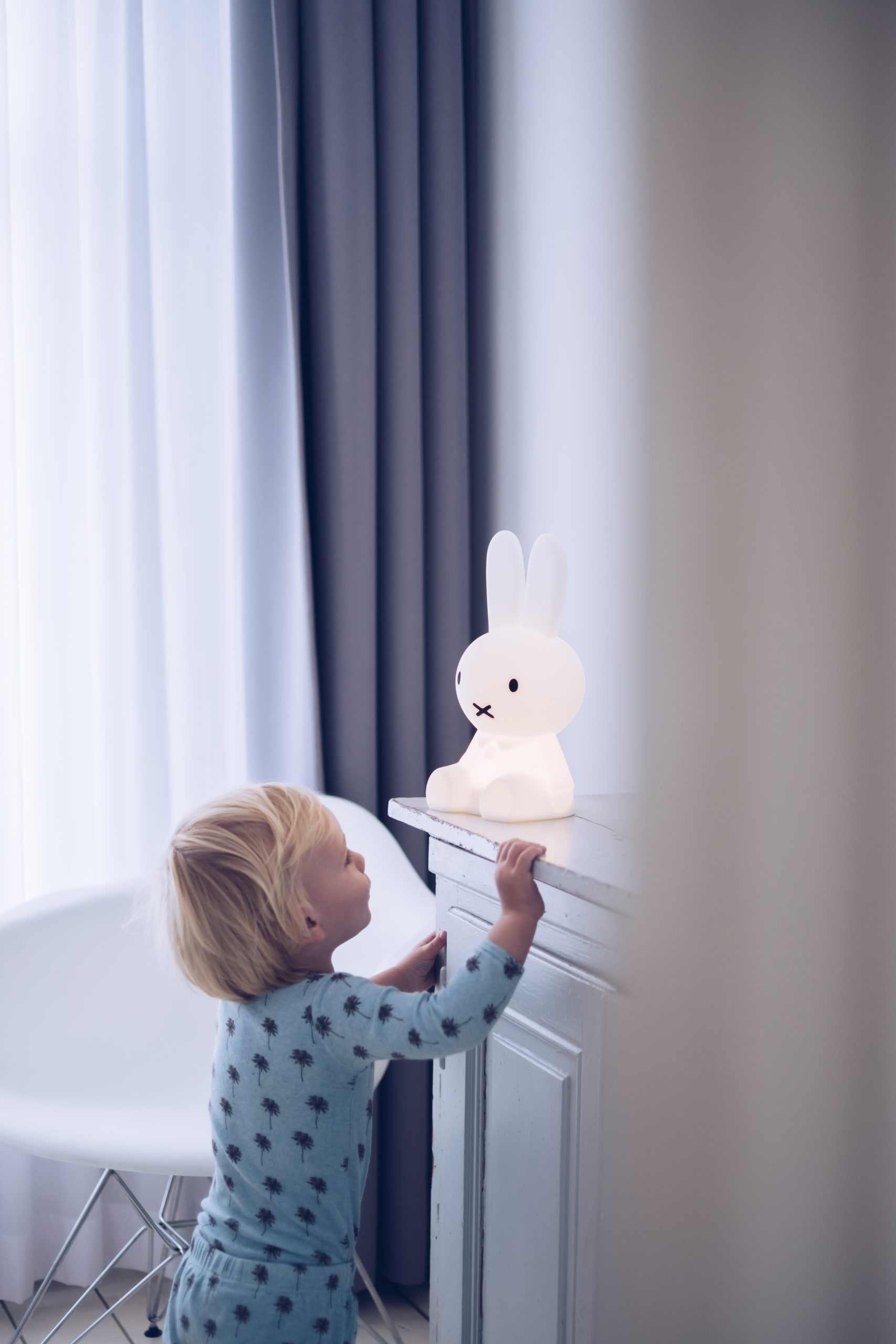 Un enfant regarde une veilleuse Miffy petit modèle blanc allumée sur une commode