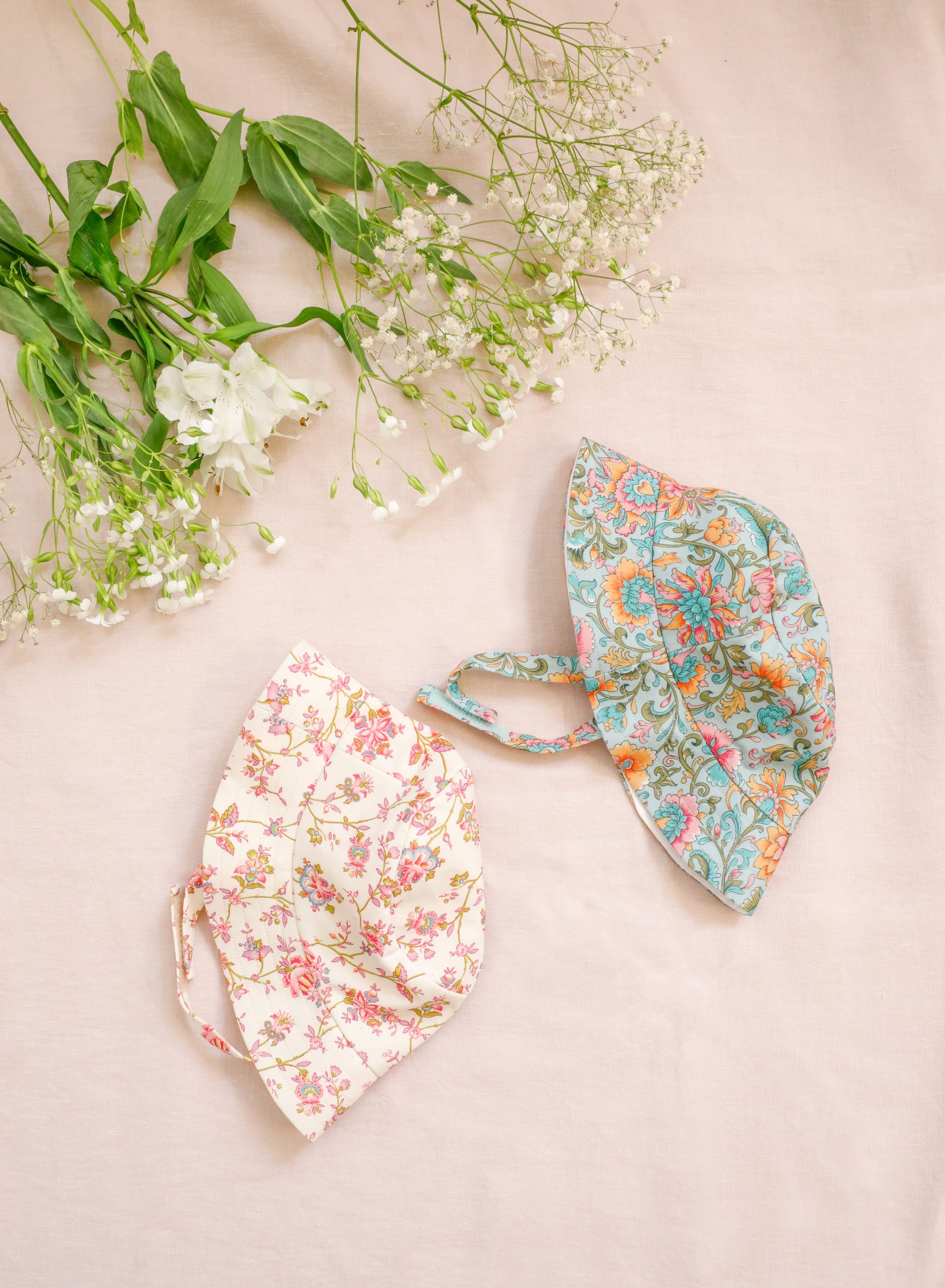 bobs Louise Misha imprimés floraux rose et bleu vert posés sur un tissu rose avec des fleurs blanches