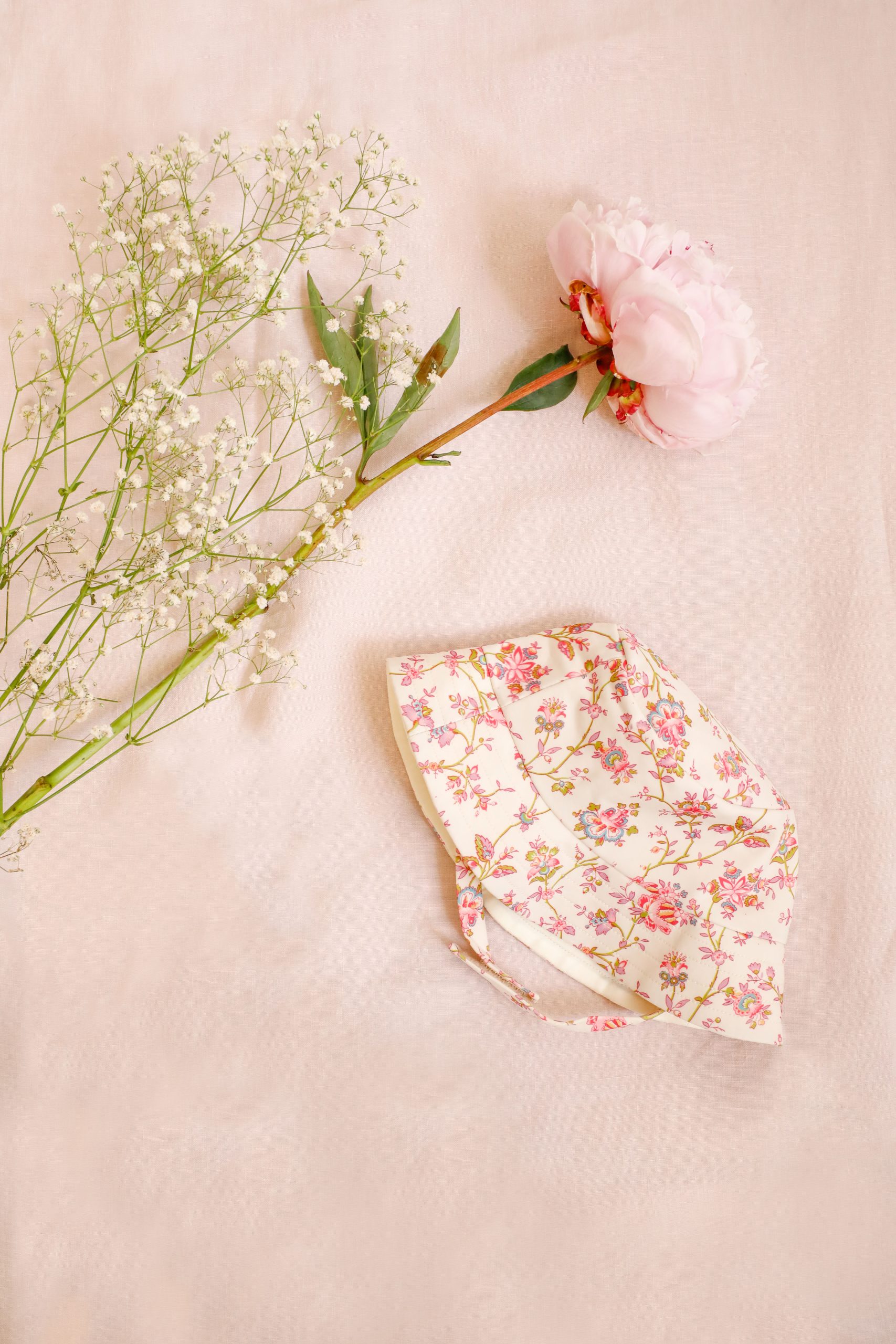 bob anti UV bébé fille Louise Misha fleuri rose posé à côté de fleurs