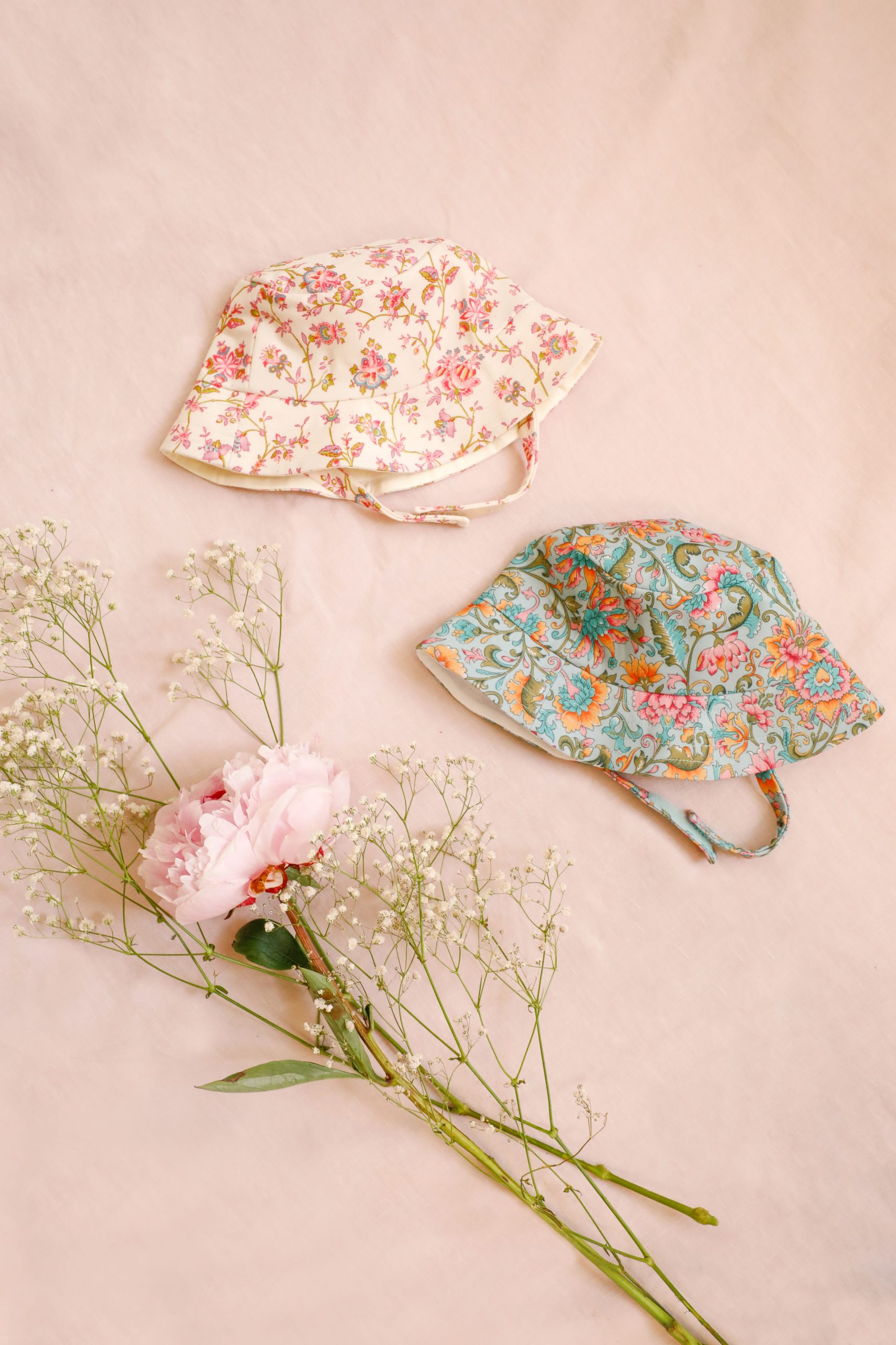 chapeaux bébé Louise Misha anti UV fleuris rose et bleu vert posés à côté de fleurs