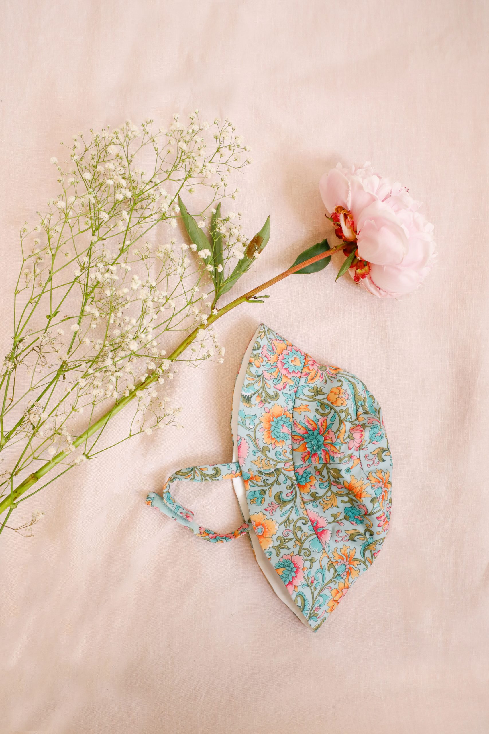 Bob bébé été anti-UV Devy bleu vert Louise Misha avec imprimé floral, vu à plat à côté de fleurs