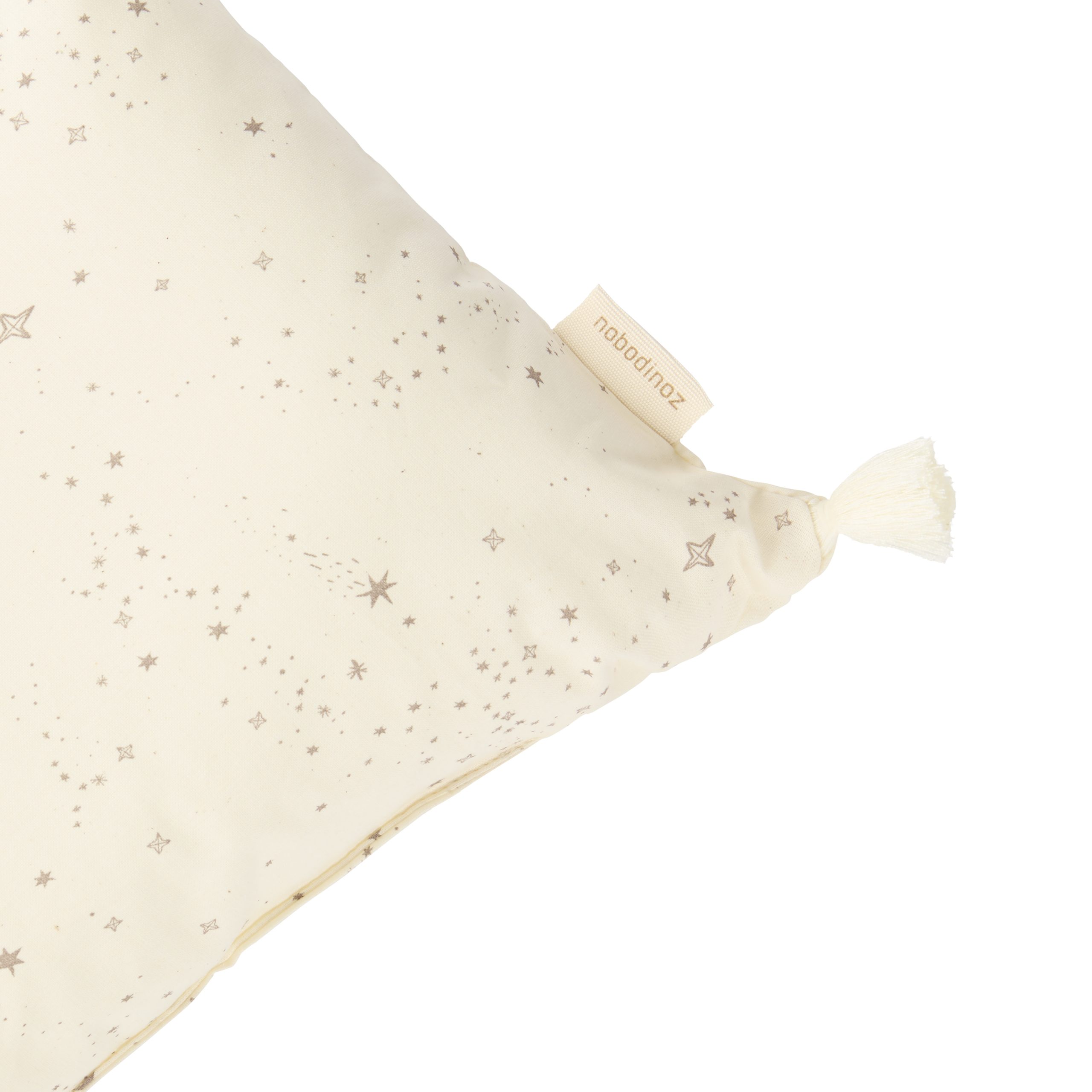 Détail du coussin rectangulaire Nobodinoz Natural avec pompon et étiquette sur tissu étoilé en coton bio