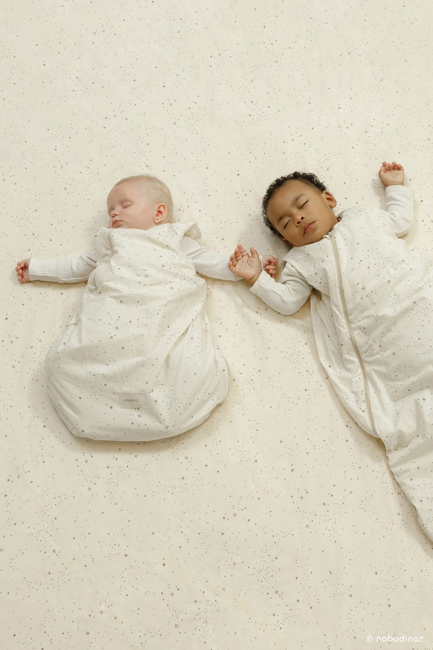 Deux bébés qui dorment dans la gigoteuse bébé Nobodinoz crème à étoiles.
