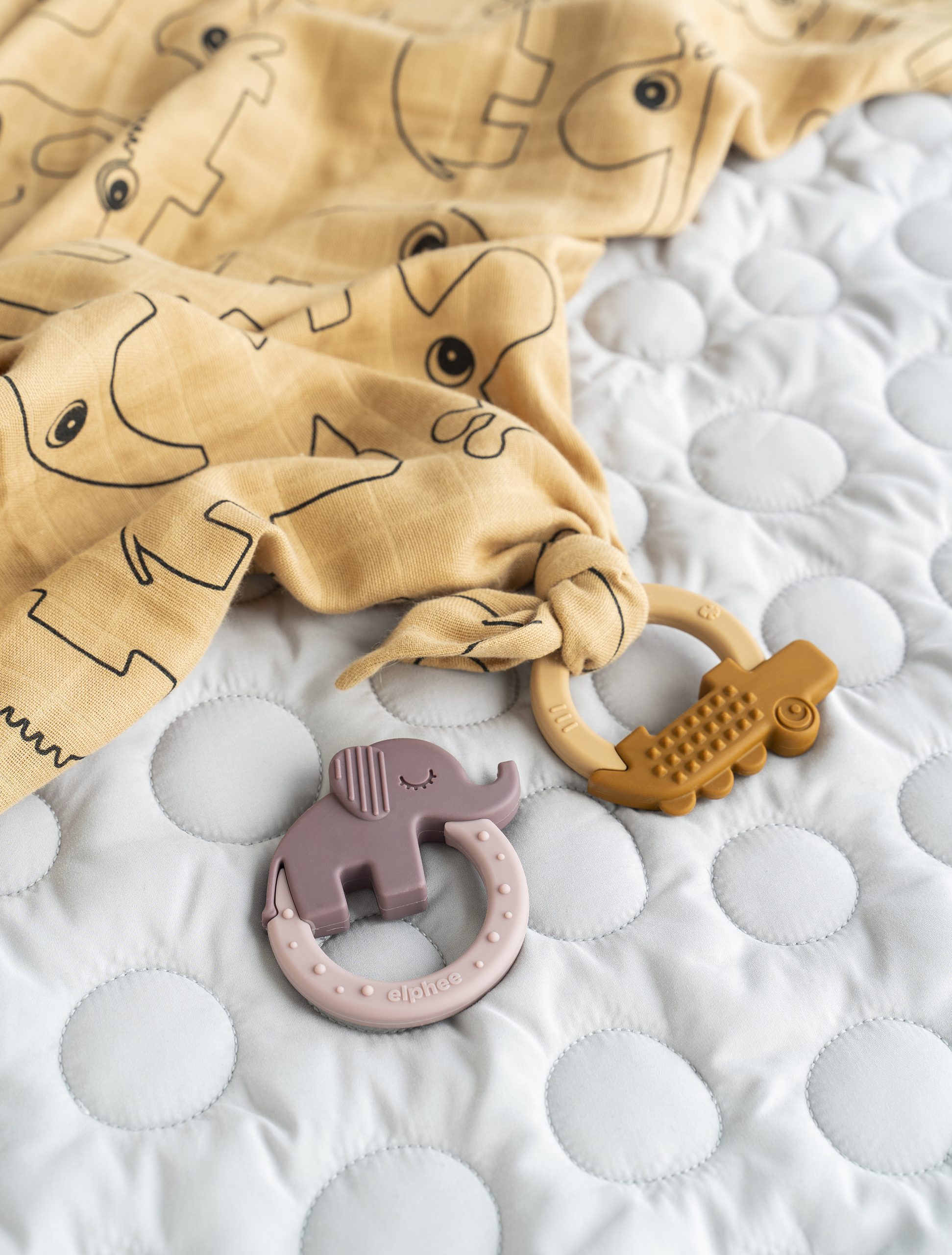 Anneaux de dentition Done by Deer sur un lit, avec un anneau attaché à un doudou en tissu