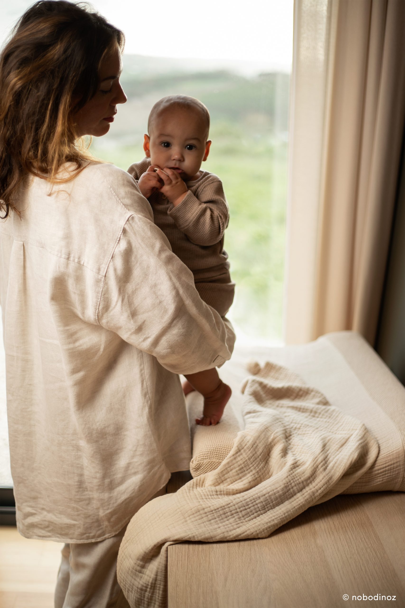 Maman tenant son bebe près d’un matelas à langer bebe dans une chambre lumineuse
