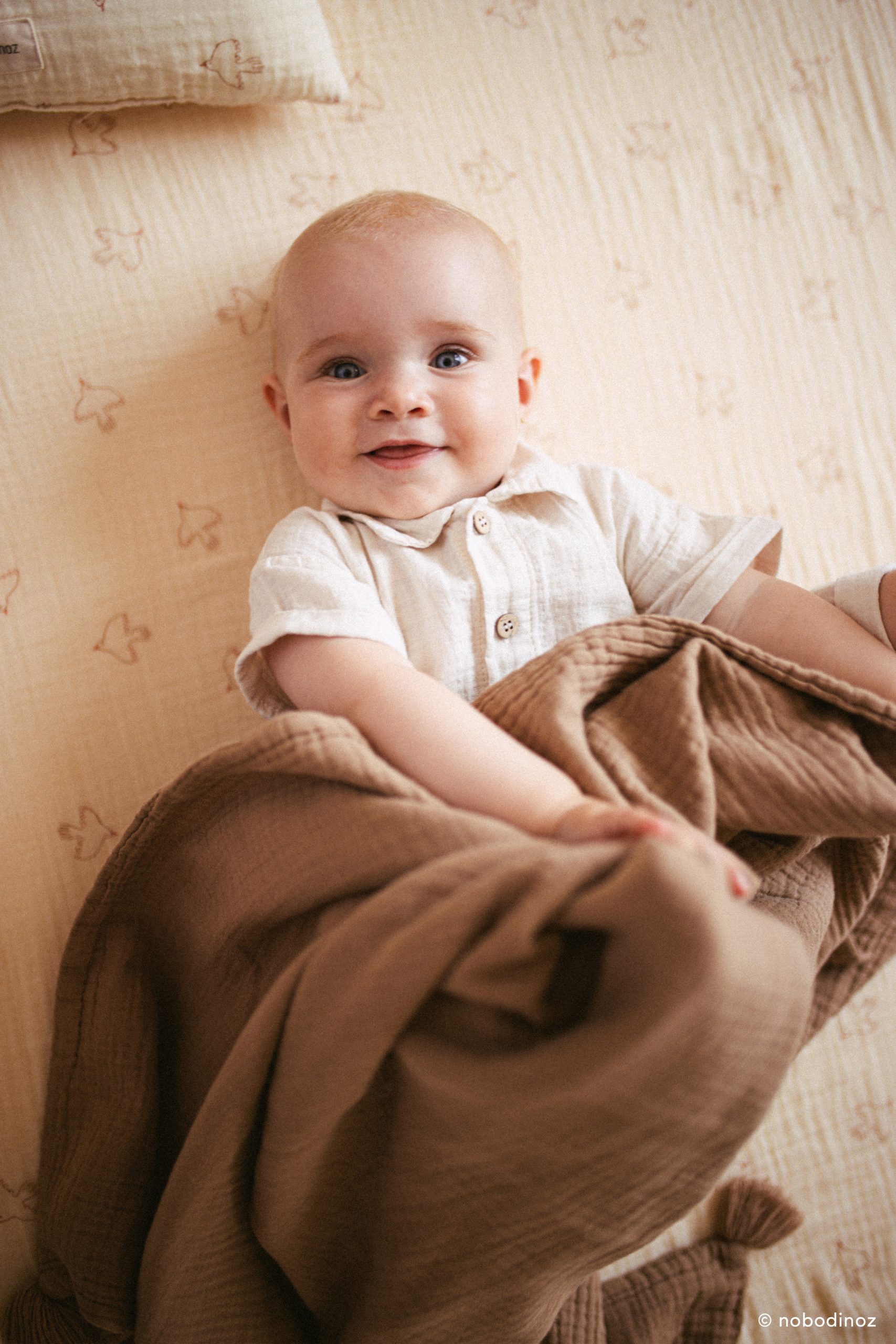 Bébé enveloppé dans la Couverture bebe Nobodinoz marron Sésame Nobodinoz en coton bio.