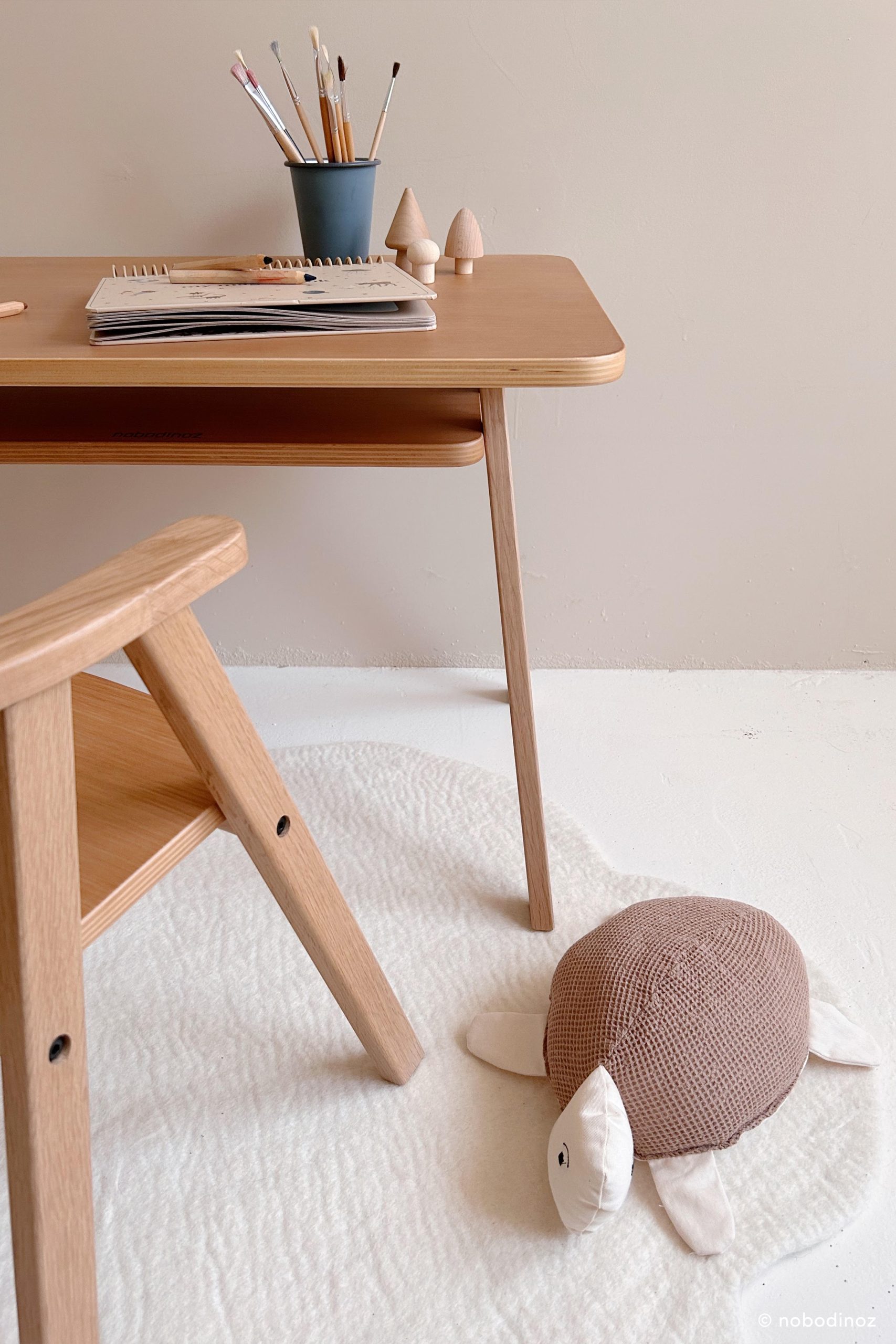 Coussin tortue bébé Nobodinoz sur tapis blanc dans une chambre en bois clair.