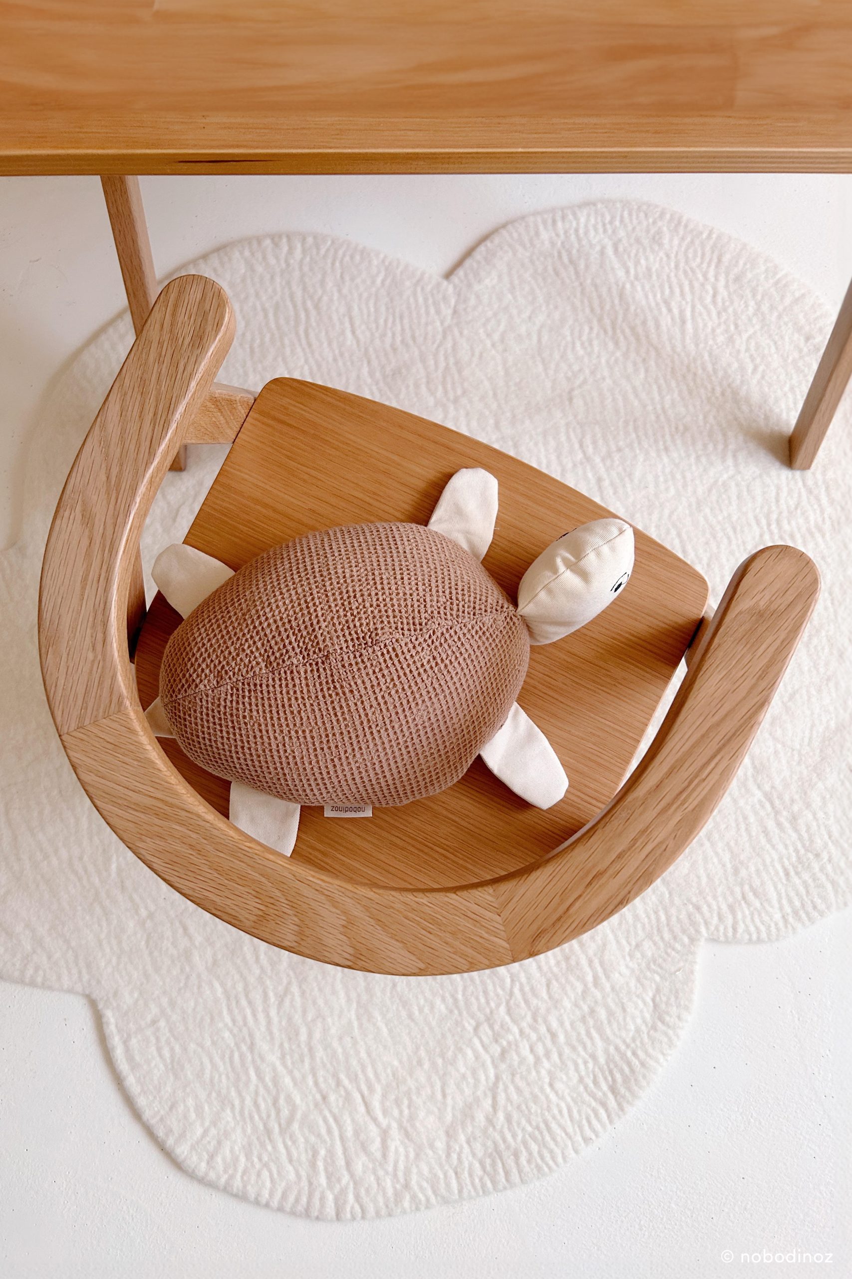 Coussin tortue Nobodinoz posé sur une chaise en bois dans une chambre bébé naturelle.
