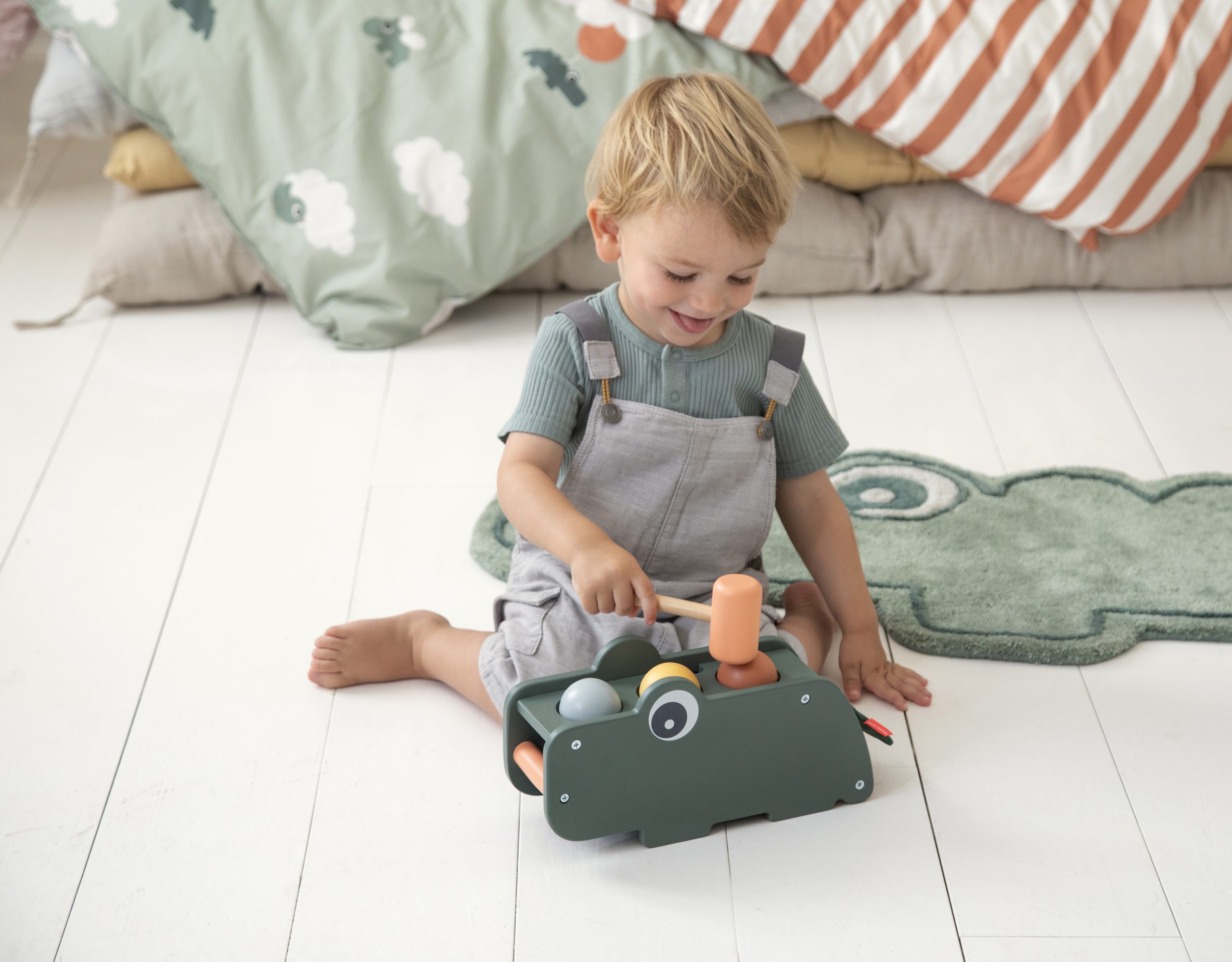 Enfant jouant avec le jeu de marteau Croco vert en bois de Done By Deer sur un tapis, jouet éducatif à partir de 1 an