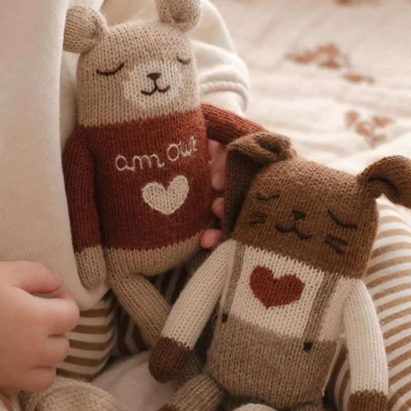Deux doudous tricotés dans les mains d’un enfant, parfaits comme cadeau de naissance doux et réconfortant