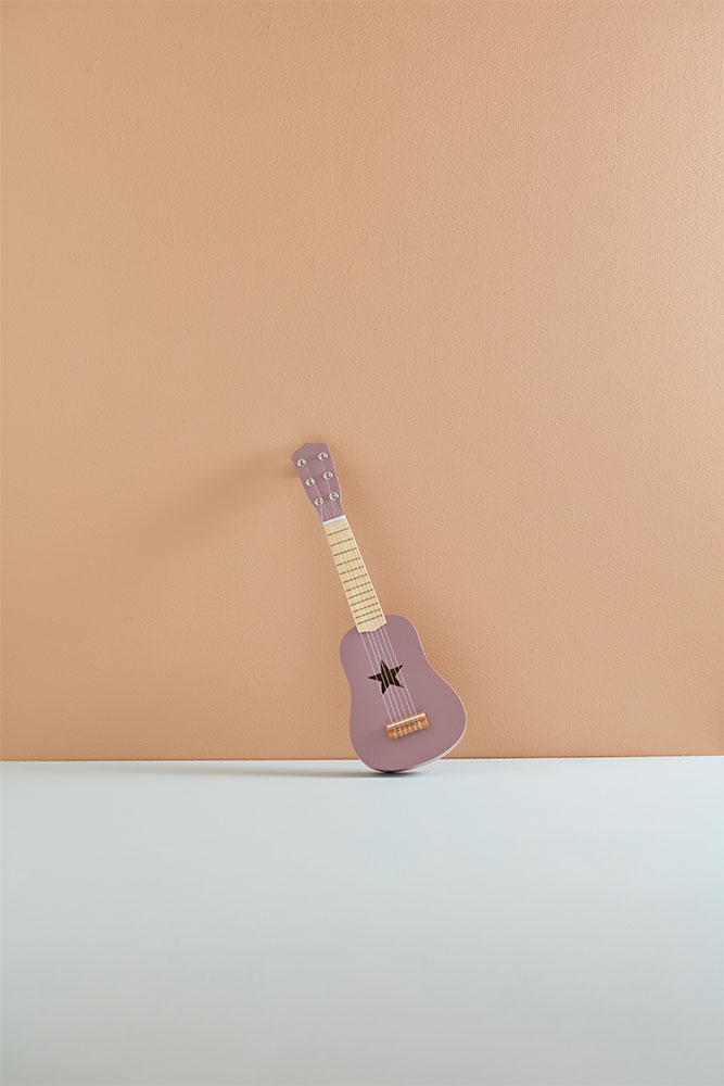 Guitare enfant 3 ans lilas en bois Kid’s Concept posée contre un mur beige