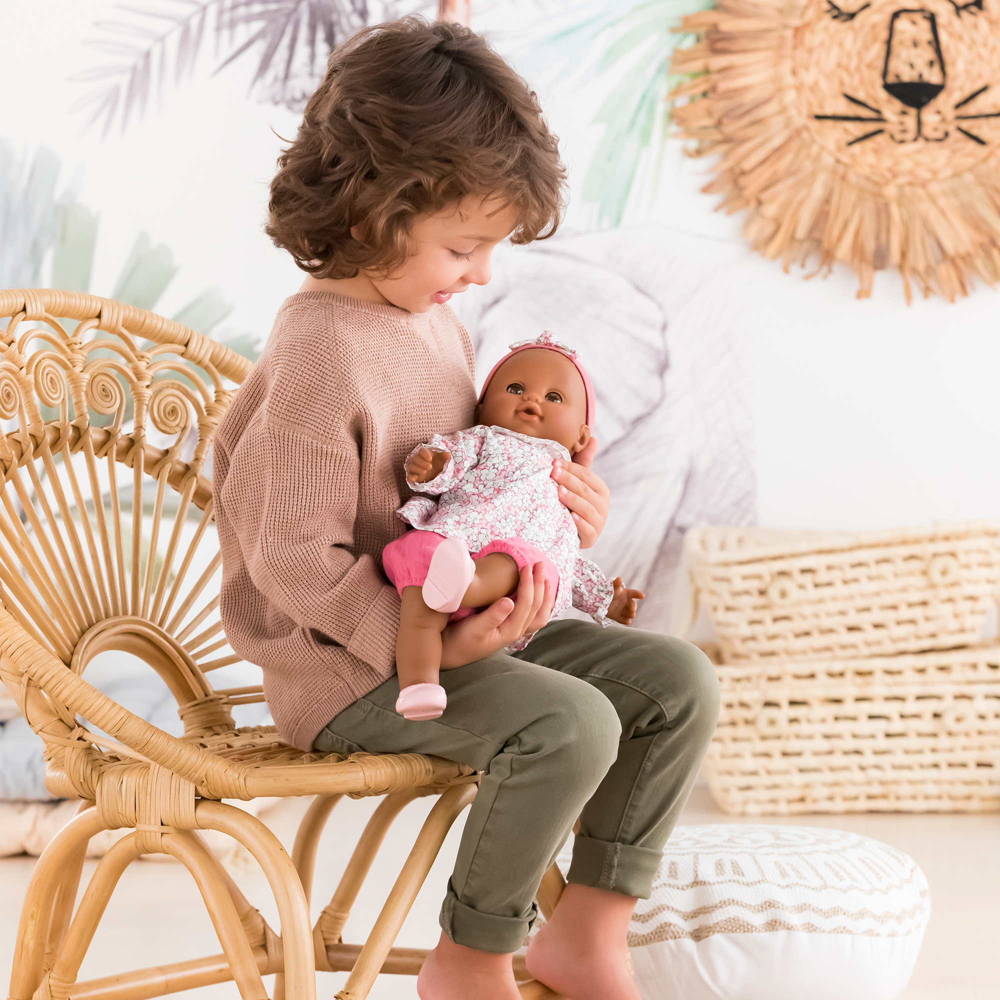 Enfant tenant le poupon Corolle Lilou assis sur une chaise en rotin.