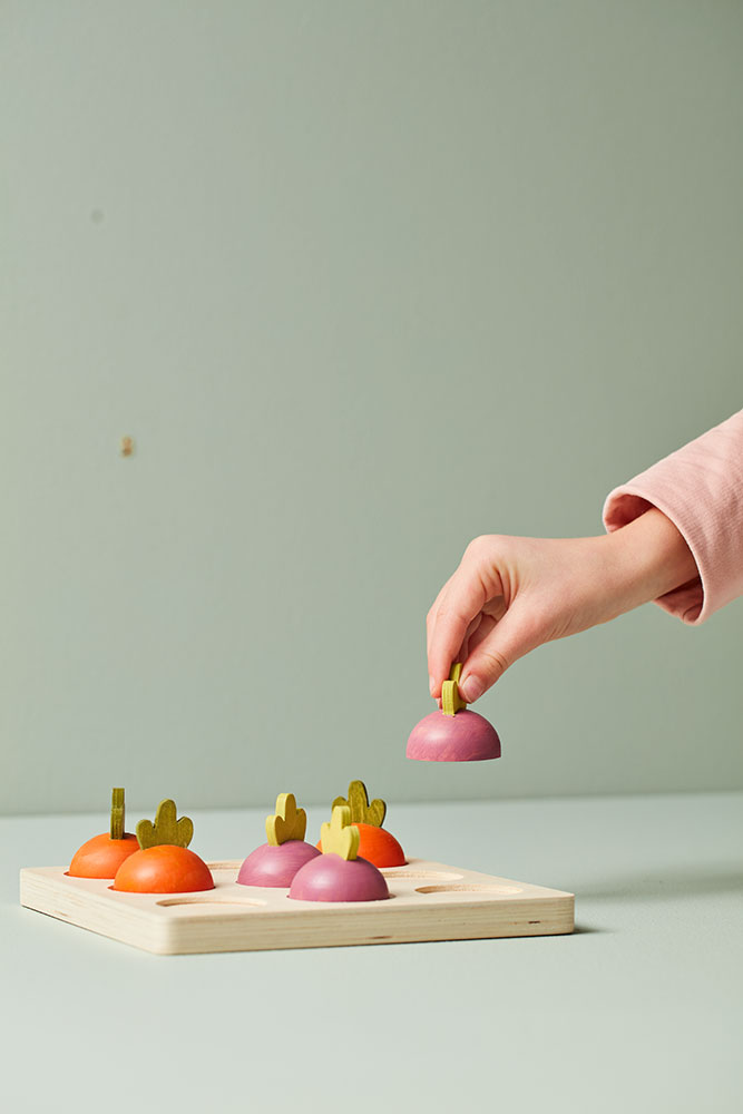 Main d’enfant soulevant un pion-légume du Jeu Tic Tac Toe en bois enfants du morpion Kid’s Concept.