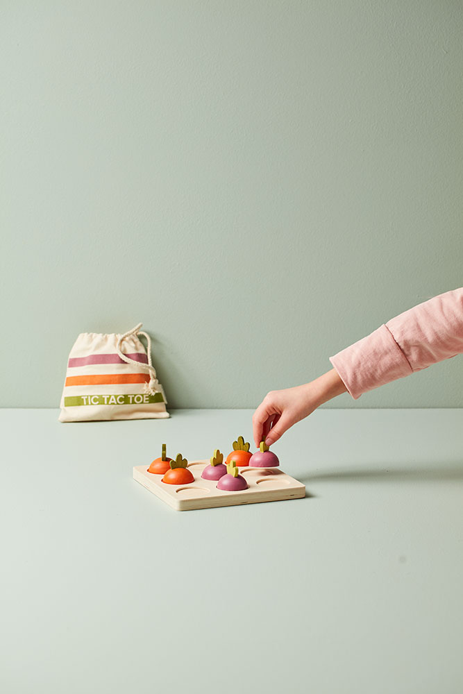 Enfant jouant avec le Jeu Tic Tac Toe en bois enfants du morpion Légumes Kid’s Concept sur une table claire.
