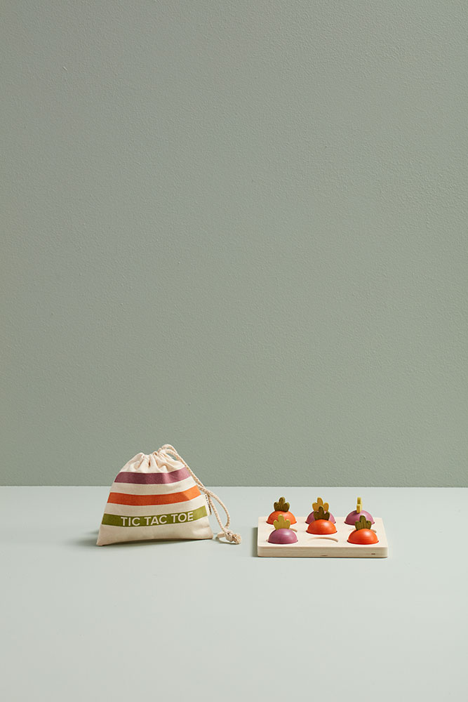 Jeu Tic Tac Toe en bois enfants du morpion Légumes Kid’s Concept présenté avec son pochon fermé sur fond vert.