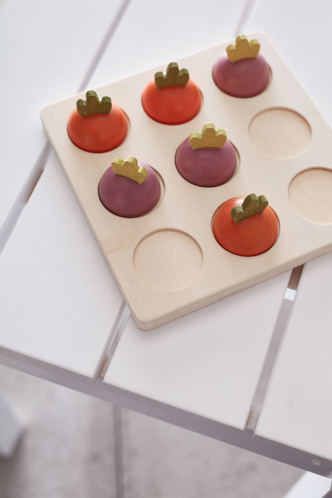 Gros plan sur le plateau en bois du morpion Légumes Kid’s Concept et ses pions colorés.