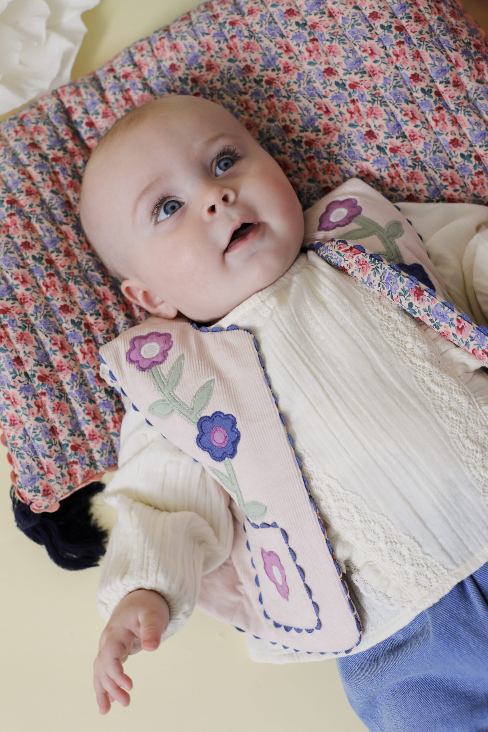 Bébé allongé portant la blouse Turbi Ivoire de Louise Misha, en gaze de coton avec volants et dentelle