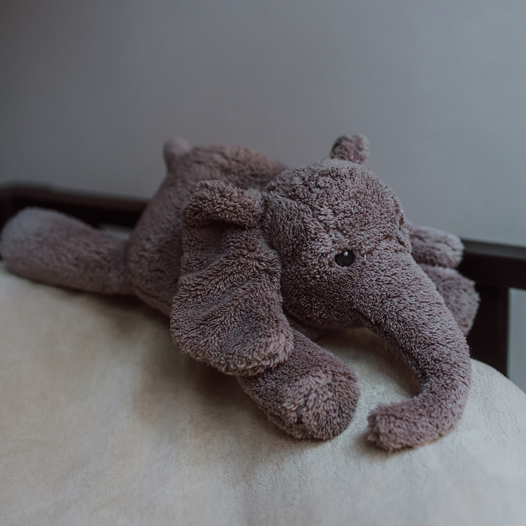 Peluche George l’Éléphant gris Flow Amsterdam vue de près, posée sur un lit – ambiance douce et réconfortante