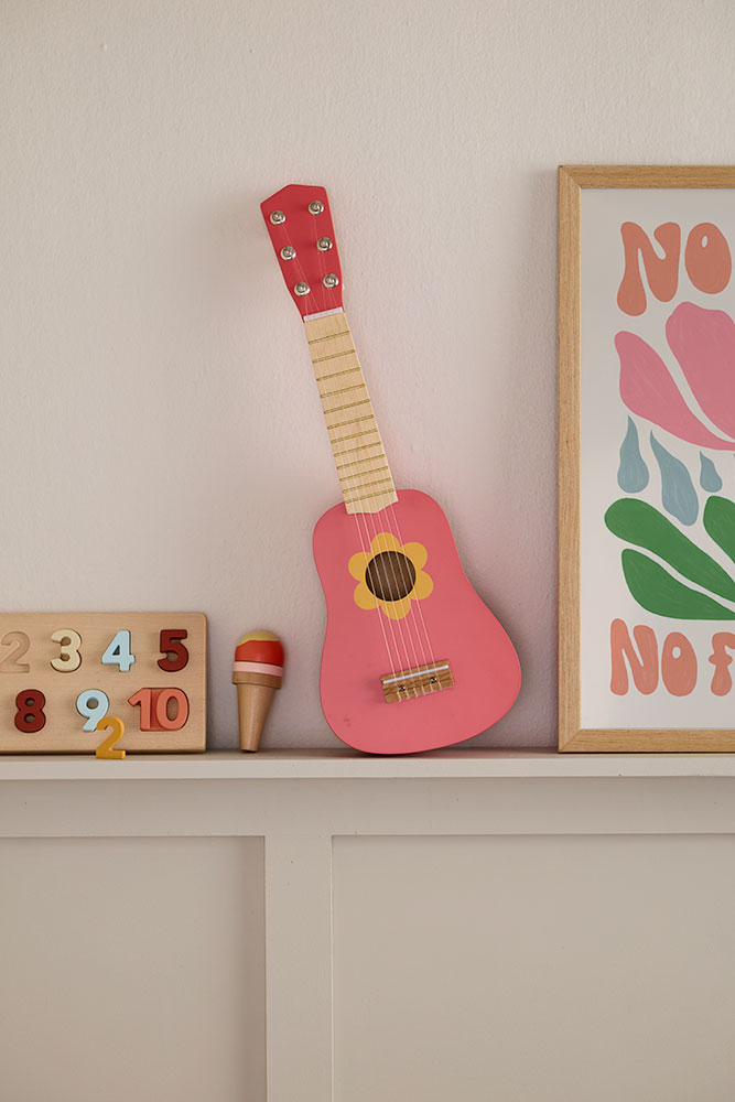 Guitare jouet Flower Pink en bois posée sur une étagère dans une chambre d’enfant