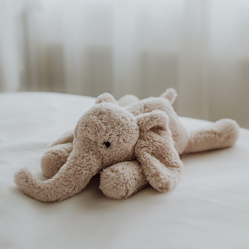 Peluche George l’Éléphant beige Flow Amsterdam posée sur un lit – ambiance douce et apaisante