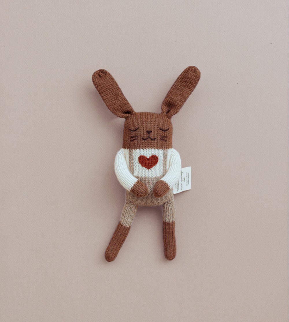 Doudou Lapin Amour Main Sauvage allongé sur fond rose – bras le long du corps – ambiance apaisée