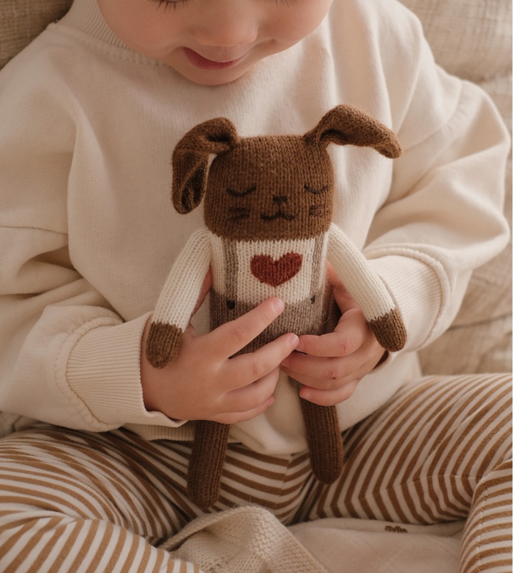 Enfant assis sur un lit tenant le doudou Lapin Amour Main Sauvage dans ses mains – vue rapprochée