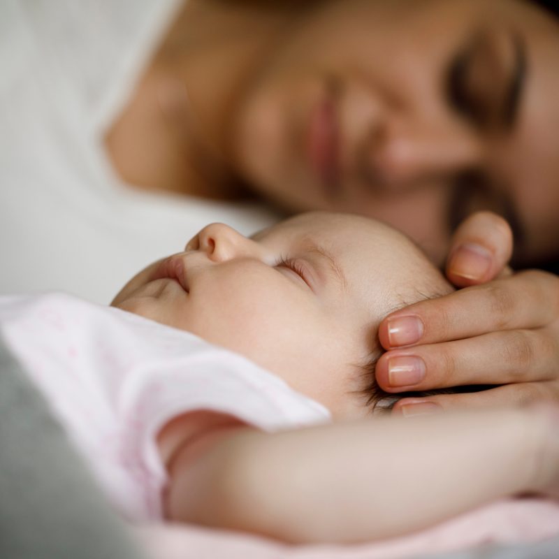 Bébé dormant paisiblement avec sa maman, main posée sur sa tête. Tout savoir sur le sommeil de bébé