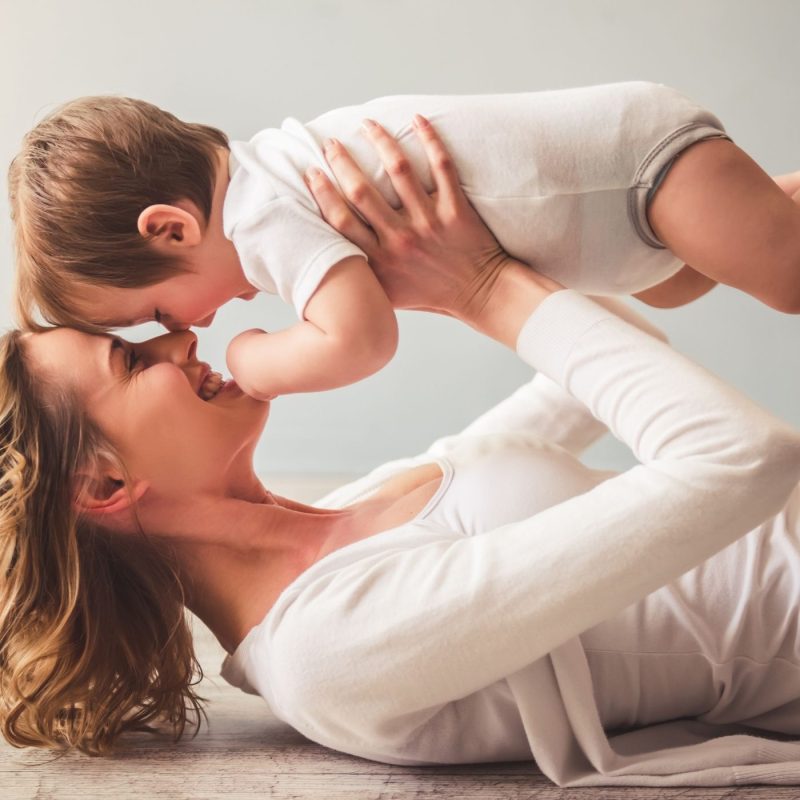 Maman jouant avec son bébé en le soulevant, scène illustrant l’éducation positive, le lien parent-enfant et la confiance.