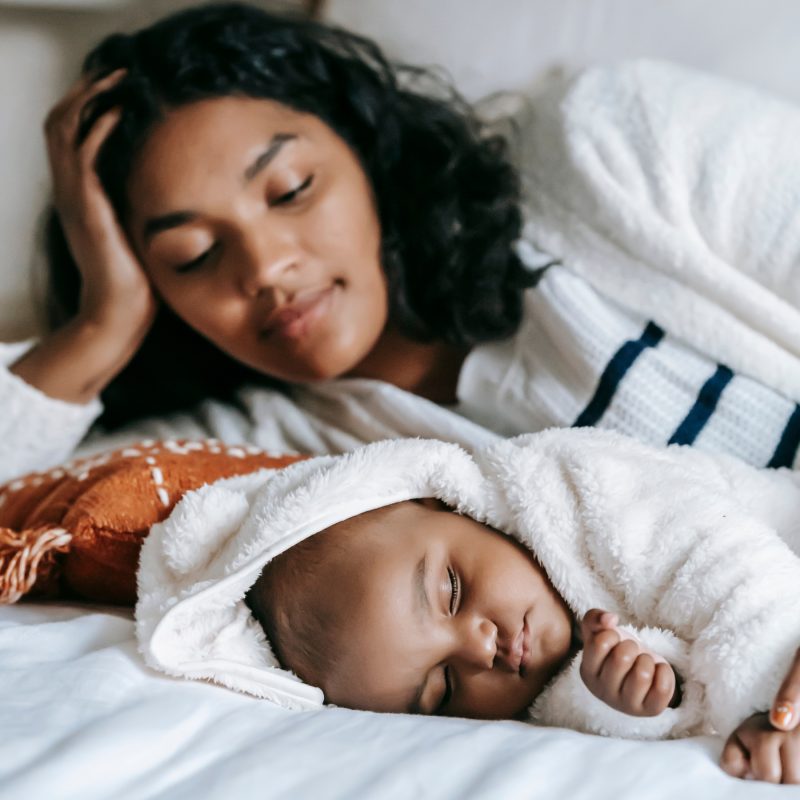 Maman allongée à côté de son bébé qui dort paisiblement dans son lit