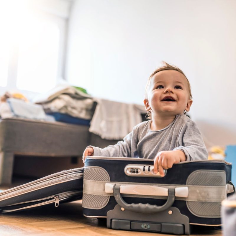 Bébé assis dans une valise ouverte dans une chambre, prêt pour partir en vacances avec ses parents