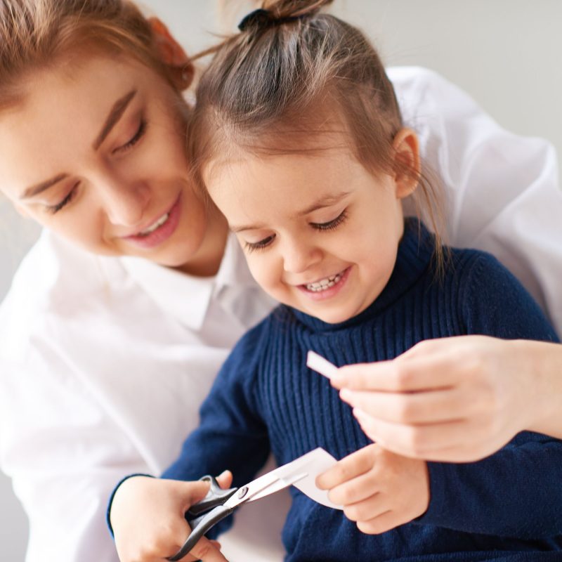 Enfant découpant du papier avec des ciseaux, aidé par sa mère, pour développer sa motricité fine