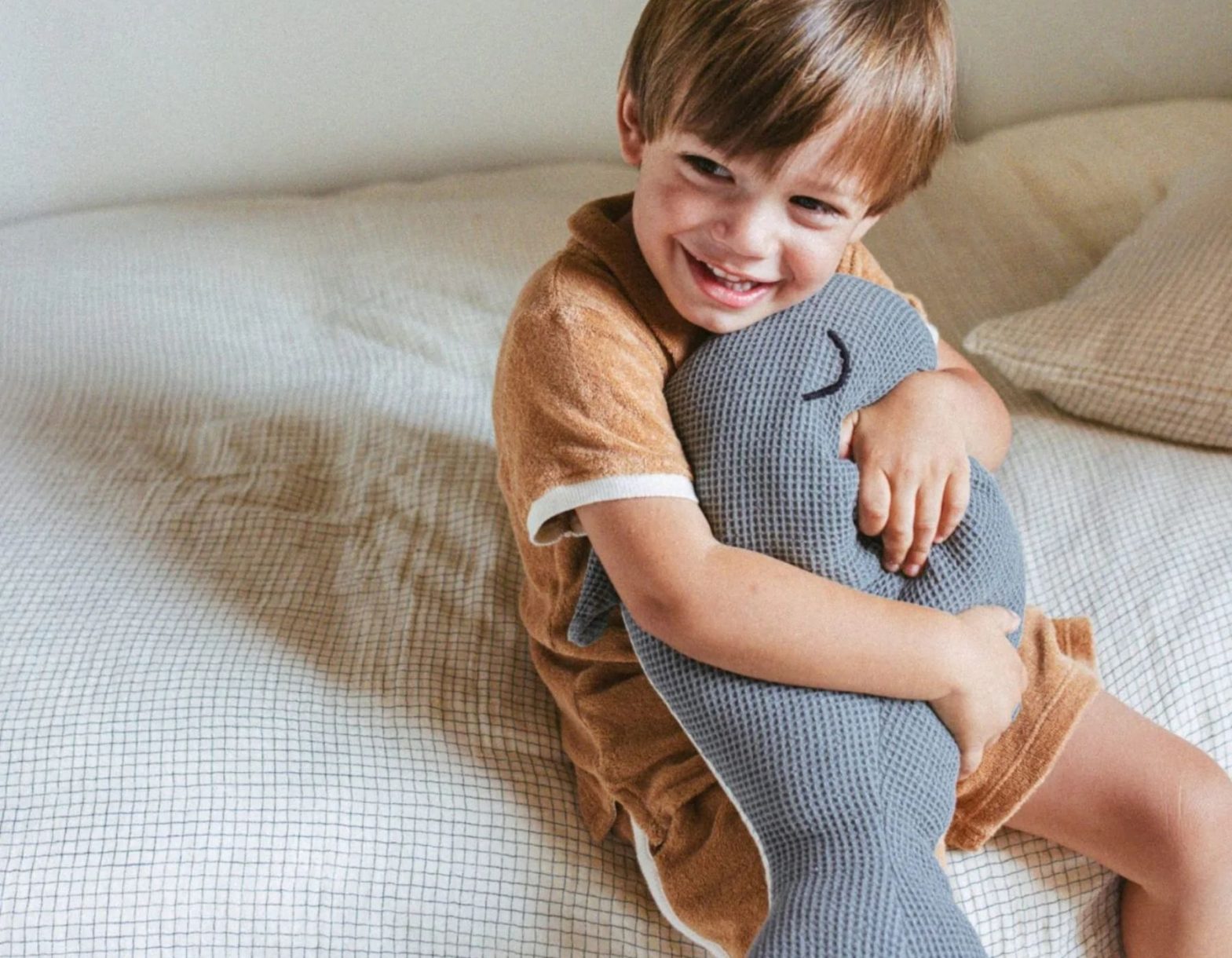 Enfant souriant câlinant une peluche baleine dans une chambre lumineuse