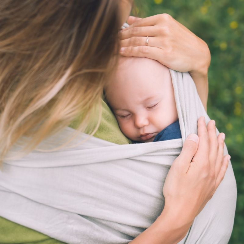 Bébé endormi dans une écharpe de portage extensible contre sa maman en extérieur