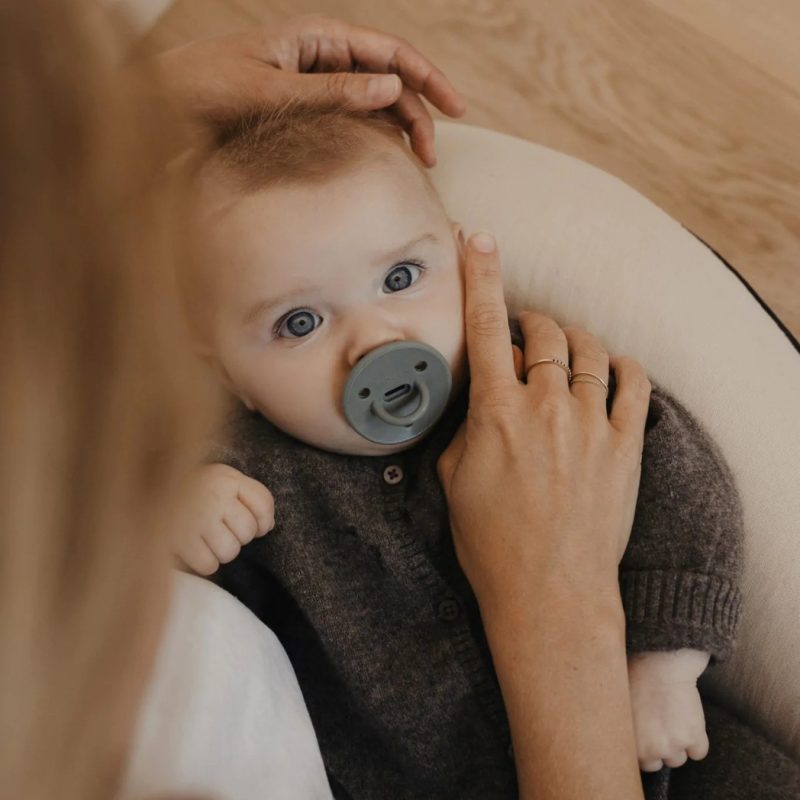 Bébé avec sucette ChooChoo Elhée Kaki dans les bras d’un parent