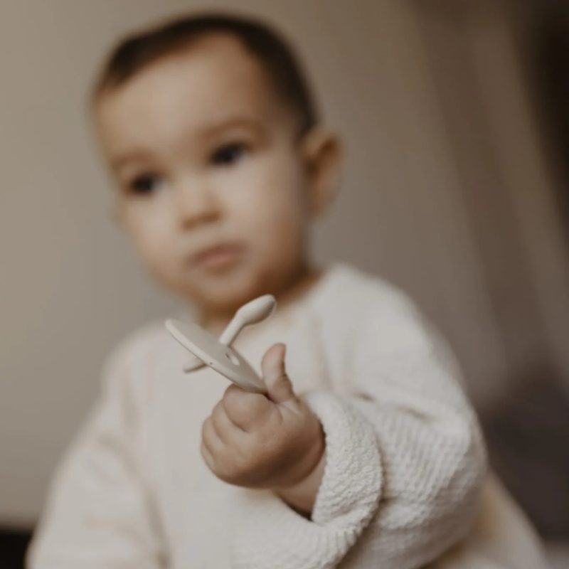 Bébé avec sucette ChooChoo Elhée beige tenue entre les doigts