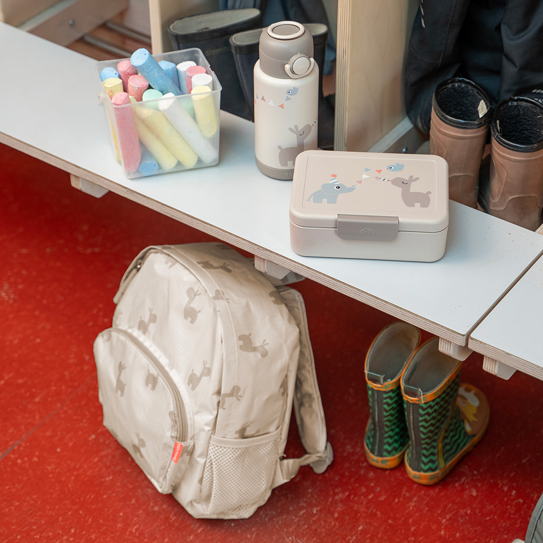Boîte à goûter sable Done by Deer avec sac à dos et gourde assortis dans une entrée de crèche