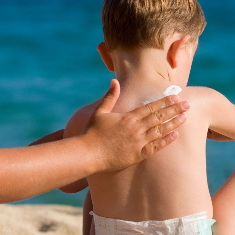 Application de crème solaire sur le dos d’un bébé à la plage