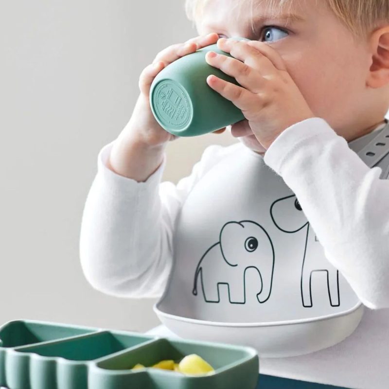 Bébé en pleine diversification alimentaire boit dans une tasse en silicone et utilise une assiette compartimentée adaptée