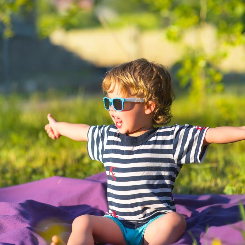 Garçon en lunettes de soleil bleues assis sur une couverture en plein soleil